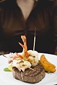 Woman holding plate of Surf & Turf (beef steak with prawns)