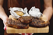 Man holding grilled beef steaks on chopping board