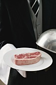 Butler serving raw beef steak on plate with dome cover