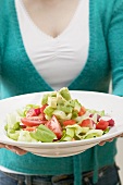 Woman holding plate of salad with avocados and tomatoes