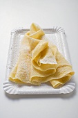 Wafer-thin crêpes with icing sugar on paper plate