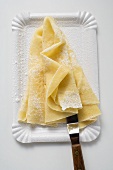 Wafer-thin crêpes with icing sugar on paper plate