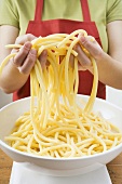 Woman lifting cooked macaroni out of bowl with her hands