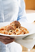 Woman holding plate of spaghetti with meatballs