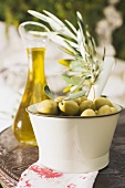 Green olives, olive sprig & olive oil on table out of doors