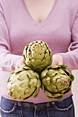 Woman holding three artichokes