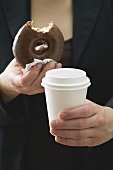 Woman holding doughnut (a bite taken) & plastic coffee cup