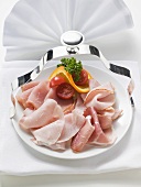 Slices of ham garnished with tomatoes and orange on plate