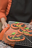 Hands holding Halloween biscuits with names on cake rack