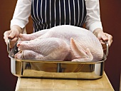 Woman holding stuffed turkey in roasting tin