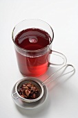 Fruit tea in glass cup, tea leaves in strainer beside it
