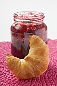 Jar of raspberry jam, croissant in foreground