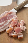 Slices of bacon & diced bacon on chopping board with knife