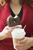 Frau hält angebissenes Schokoladendoughnut und Kaffeebecher