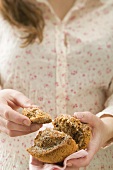 Woman holding halved muffin on checked napkin