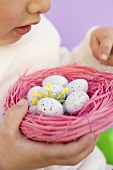 Child holding Easter eggs in pink nest