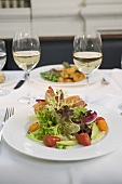 Salad with bacon and glasses of white wine on laid table