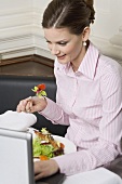 Woman eating salad while working on laptop in restaurant