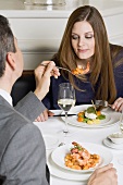 Man offering woman prawn on fork in restaurant