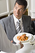 Waiter serving gnocchi with prawns to man