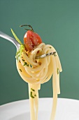 Spaghetti with cherry tomato on fork above white plate