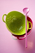 Coloured colanders, stacked, and pink cooking spoon