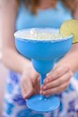 Woman holding a lime cocktail in a turquoise glass