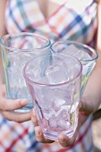 Woman holding three glasses filled with ice cubes