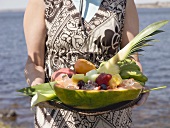 Woman holding tray of fresh exotic fruit by sea