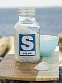 Sea salt in bottle on chopping board, sea in background