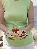 Woman holding plate of crab claws and dip on beach