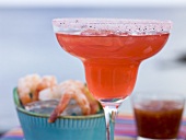Red cocktail in glass, shrimps with dip in background