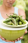 Woman holding grilled chillies on top of a green bowl