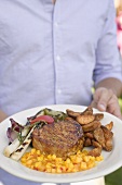 Man holding plate of grilled steak and accompaniments