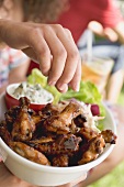 Hand reaching for grilled chicken wings