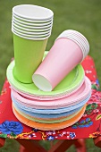 Coloured paper cups and plates on folding stool in garden