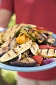 Person holding a plate of grilled vegetables