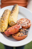 Person holding plate of grilled corn on the cob & tomatoes