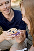 Man handing woman a blueberry muffin