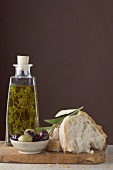 Thymianöl in Flasche, Oliven und Weißbrot auf Schneidebrett