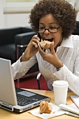 Frau isst Muffin bei der Arbeit am Computer