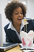 Frau im Büro isst asiatisches Nudelgericht