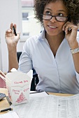 Frau im Büro mit asiatischem Nudelgericht beim Telefonieren