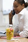 Fruit salad in plastic container, woman on telephone in background