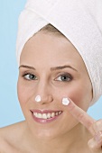 Frau tupft Gesichtscreme auf Nase und Finger