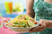 Woman holding plate with two chicken tacos