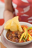 Woman serving chili con carne with nachos and peppers