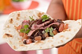 Woman holding fajita with beef, beans and tomatoes