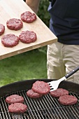 Man placing raw burgers on barbecue grill rack