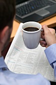 Geschäftsmann trinkt Kaffee beim Zeitunglesen im Büro